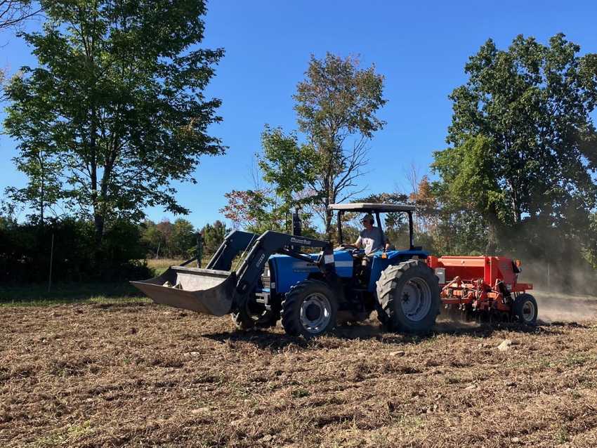 Blue tractor with orange/redish grain drill in field seeding cover crops